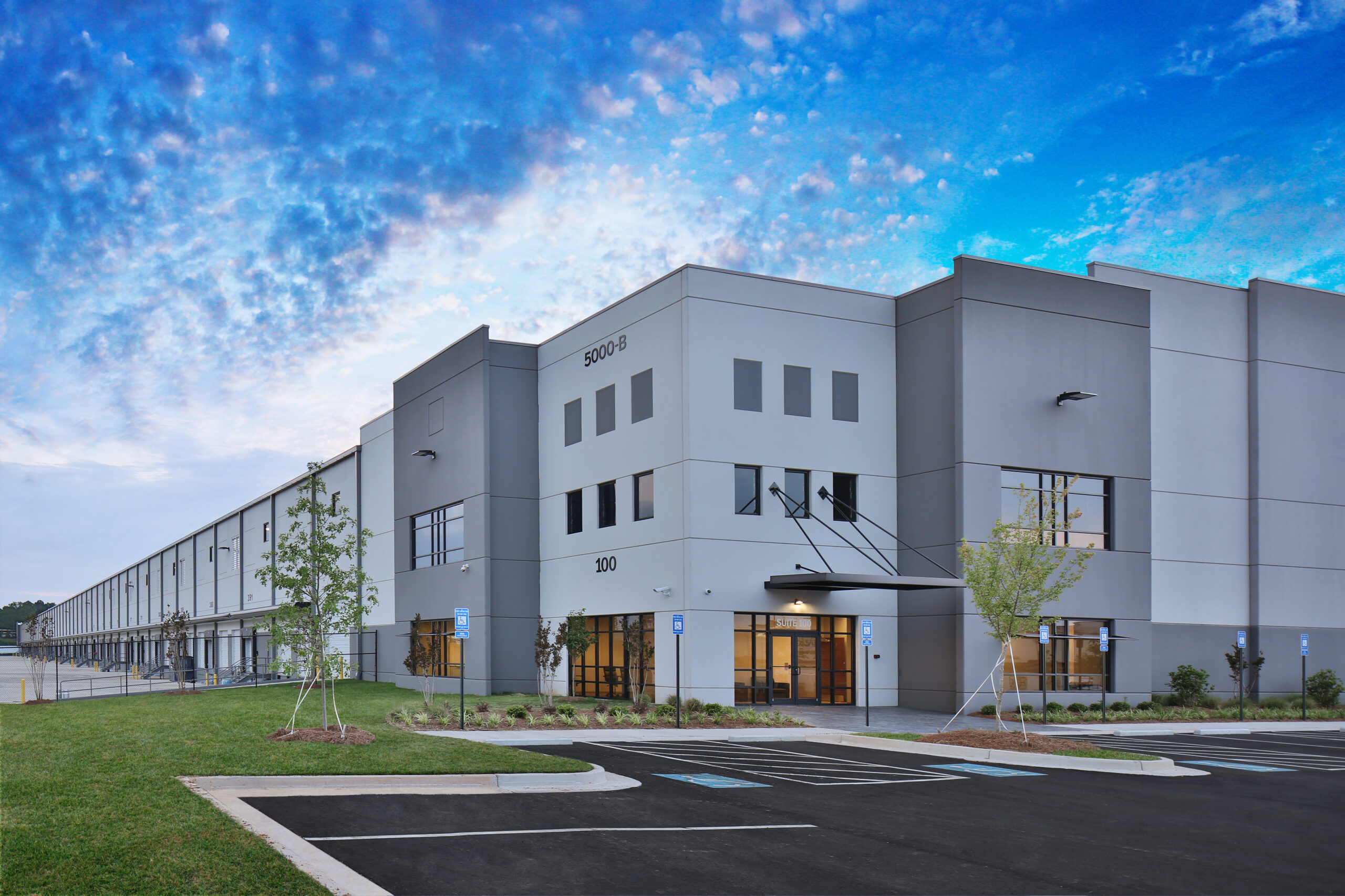 Modern gray industrial warehouse distribution building and parking lot under beautiful blue and pink cloudy sky