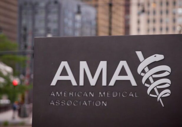 Close-up of the American Medical Association AMA exterior sign with caduceus logo against an urban city background with buildings and street traffic