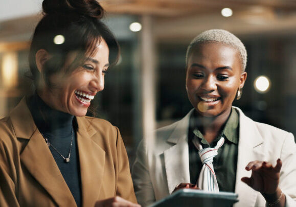 Women, tablet and team at window in office at night, happy or funny chat at finance company. Business people, tech and app at glass wall, feedback report or laugh with asset management at agency.