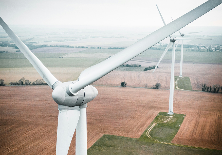 Aerial view of two wind turbines rising above agricultural fields on an overcast day, illustrating the scale of a wind farm construction project.
